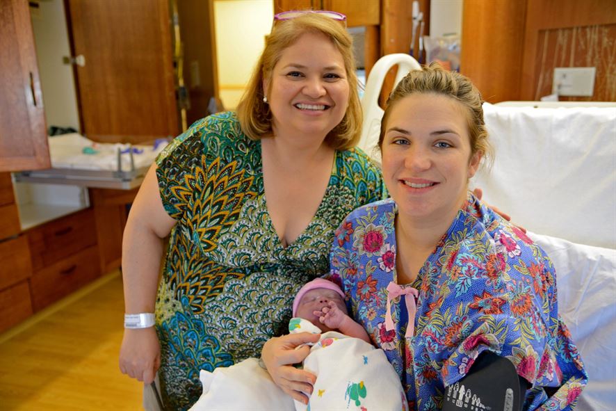Two women smiling. One woman is holding a newborn baby.