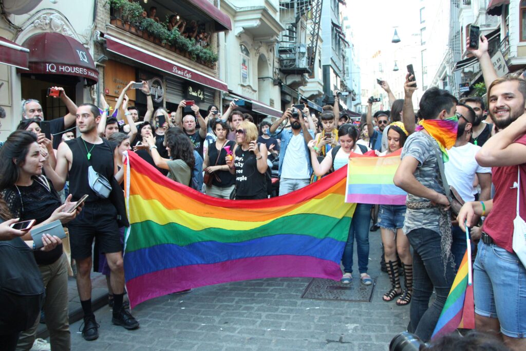 A large group of people surrounded by the colorful LGBTQ flag.