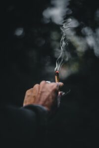A hand holding a cigar with smoke blowing away.