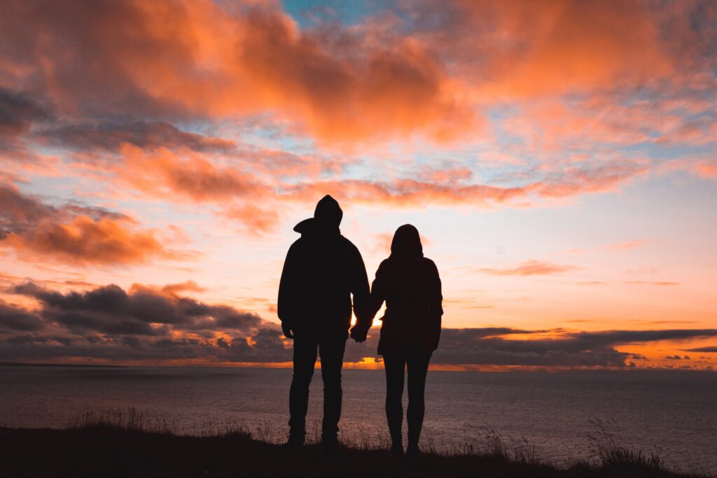 Two persons holding hands in front of a sunset.