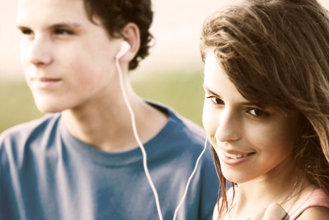 Two persons smiling and sharing earphones.