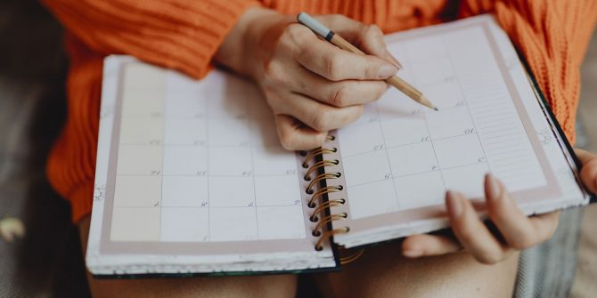 A person holding a pencil on top of an open calendar planner.