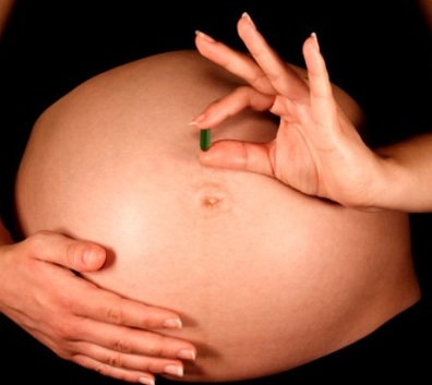 Person's hands holding pregnant belly. One hand is holding a green pill.