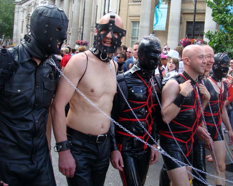 A group of people wearing leather suits and red rope tied around their bodies. Some of the persons are wearing leather masks and chains.
