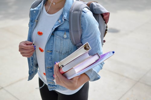 Person with backpack holding binders and books.