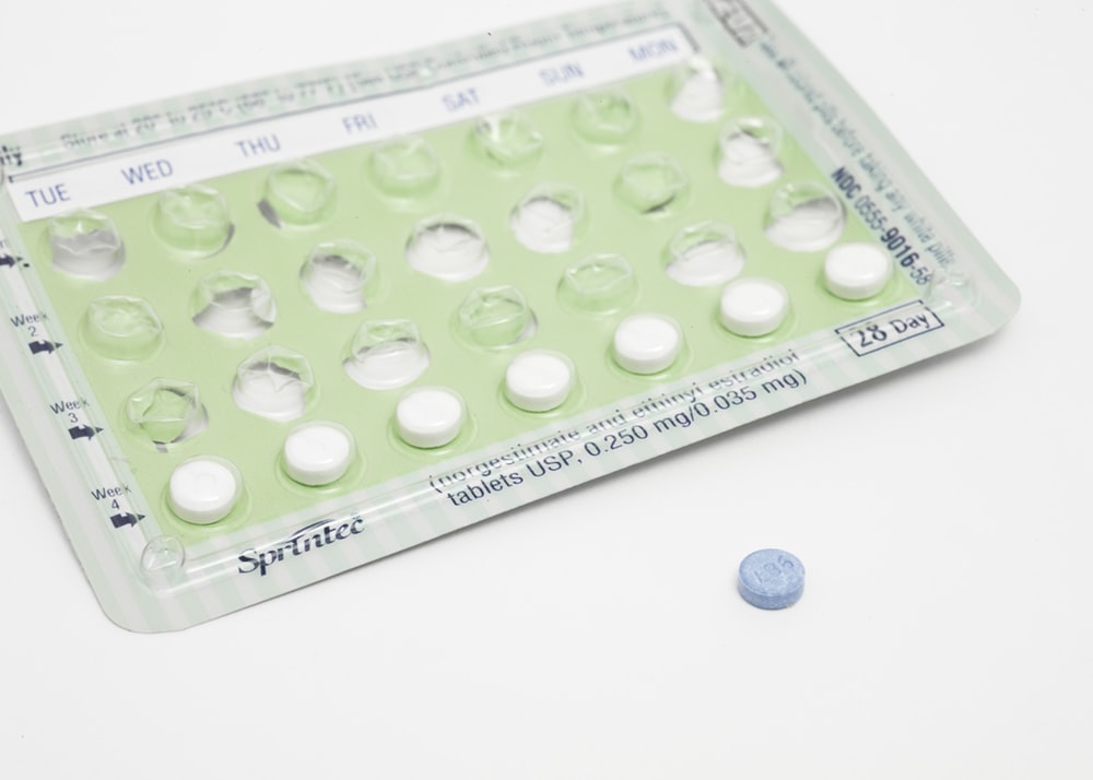 Green birth control packet against white background with single blue pill
