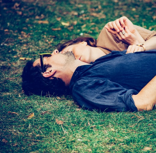 A couple laying on the grass and holding hands.
