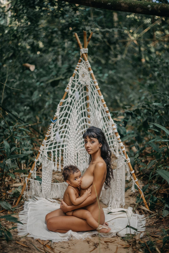 A nude woman breastfeeding a baby.