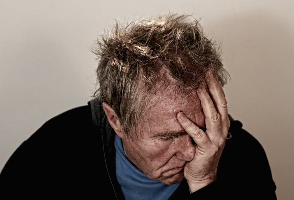 An older person with their head tilted downward and their hand against their face.