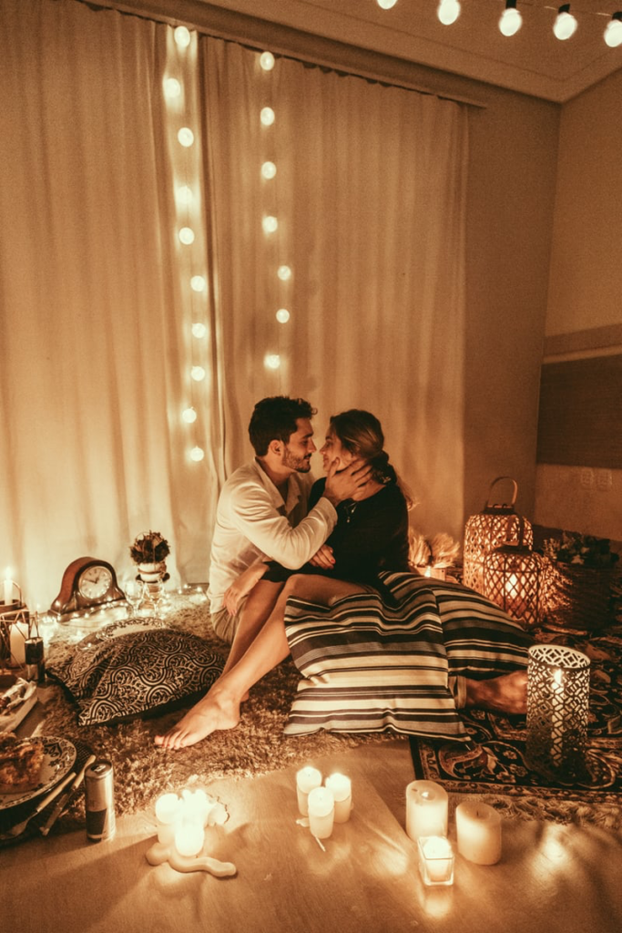 A man and woman holding each other in a romantic room lit by candles