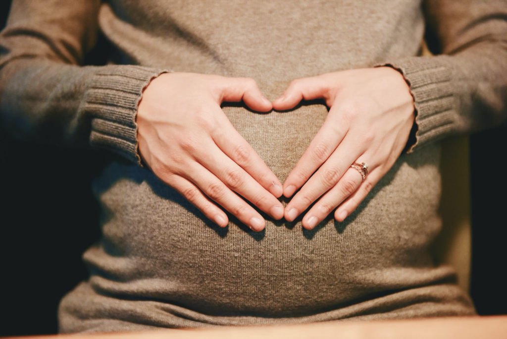 A person's hands forming a heart over their pregnant belly.