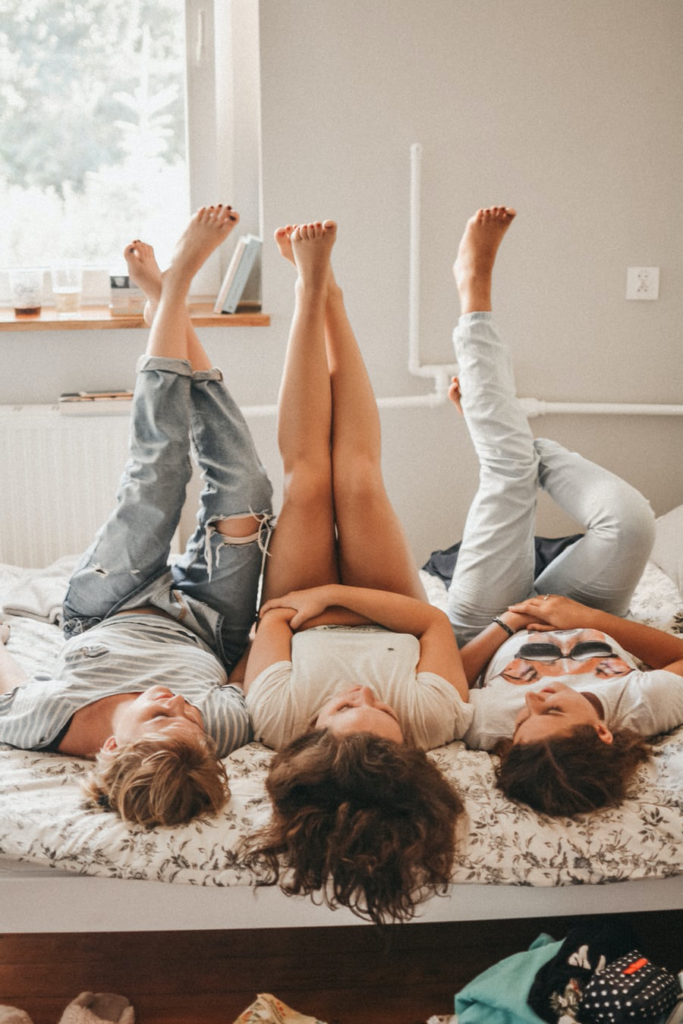 Three girls who are friends lying down next to each other with their legs up and feet towards the ceiling