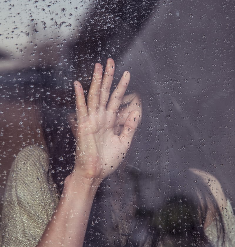 A woman with her hand on a window.