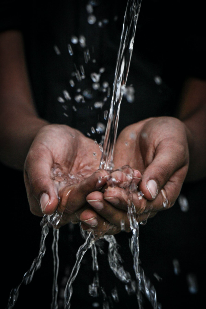 A person's hands cupped together holding dripping water.