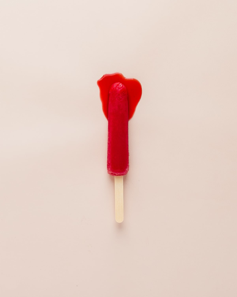 A red popsicle on a stick. The popsicle is dripping red liquid and resembles a bloody tampon.