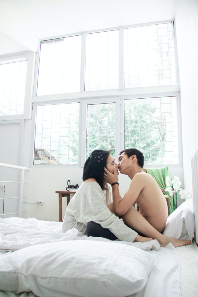 A couple sitting on a bed and kissing on the mouth.