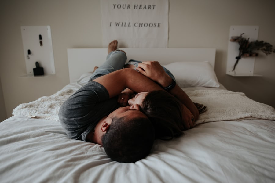 A couple laying on a bed and hugging.