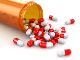 Pill bottle spilling red and light grey oblong pills onto a white table.