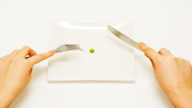 Person holding a knife and fork on top of a plate. On the plate, there is one pea. 