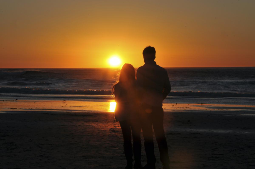 Two people walking along the beach at sunset. 