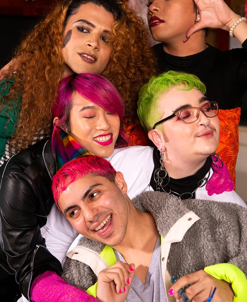 Five people with colorful hair smiling and hugging one another.