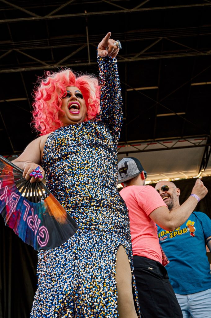 A person with pink hair and a rainbow dress pointing. 