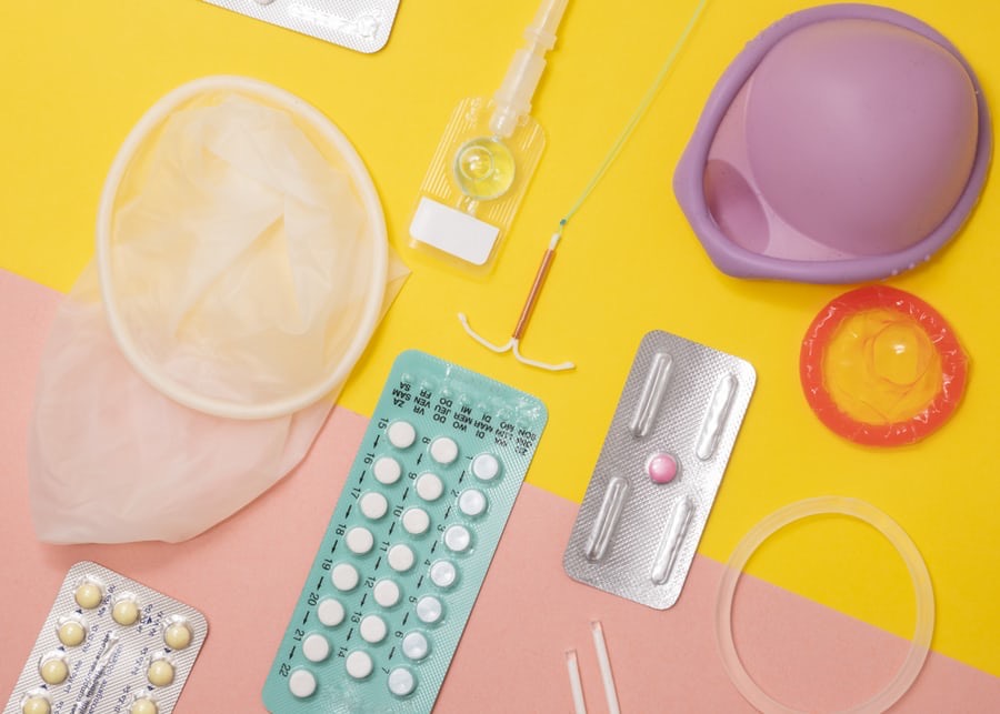 A variety of contraceptives: condoms, vaginal ring, birth control pills, intrauterine device, and arm implant.