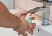 A person's hands holding a bar of soap under a sink with running water