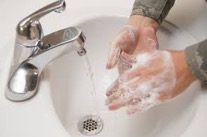 A person washing their hands under a sink with running water.