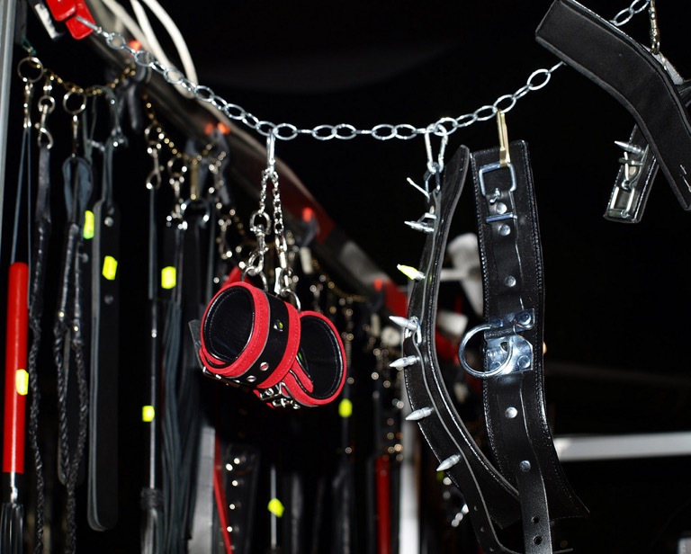 A collar, handcuffs, and leashes hanging on a chain.