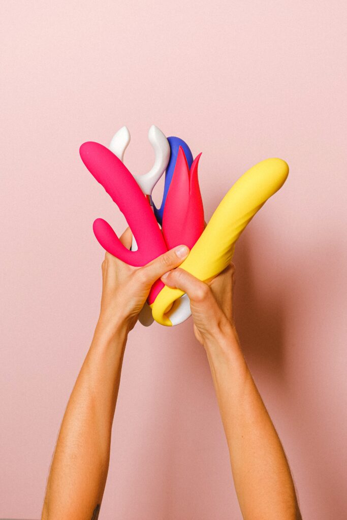 A person holding a variety of colorful vibrators and dildos.