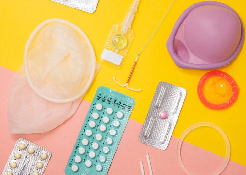 Condoms, birth control pills, iud, and other forms of birth control against a yellow and pink background