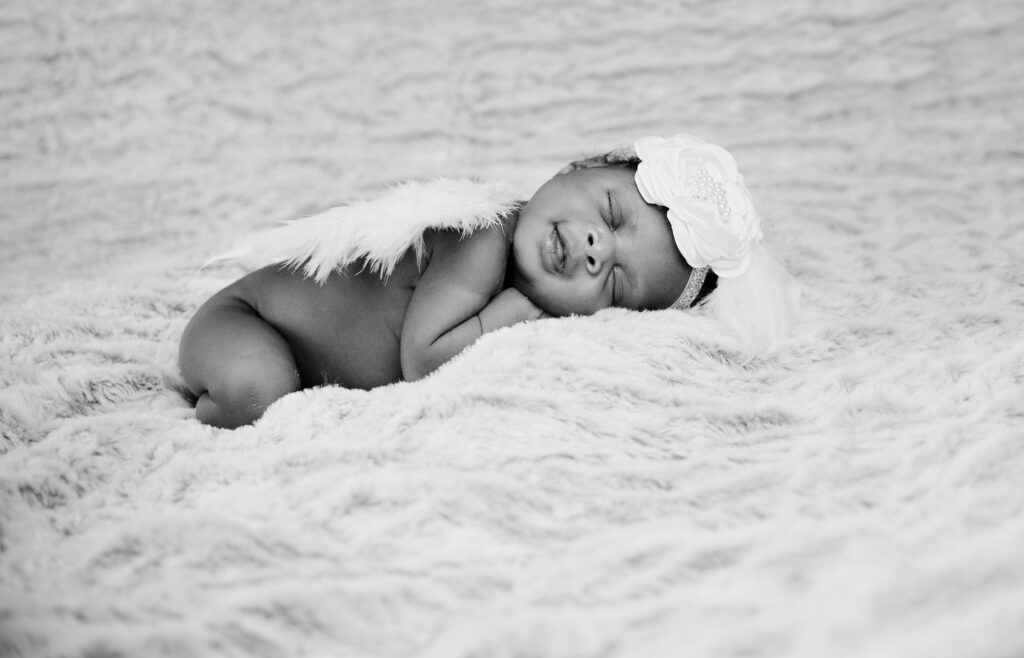 A newborn baby laying down, wearing angel wings.