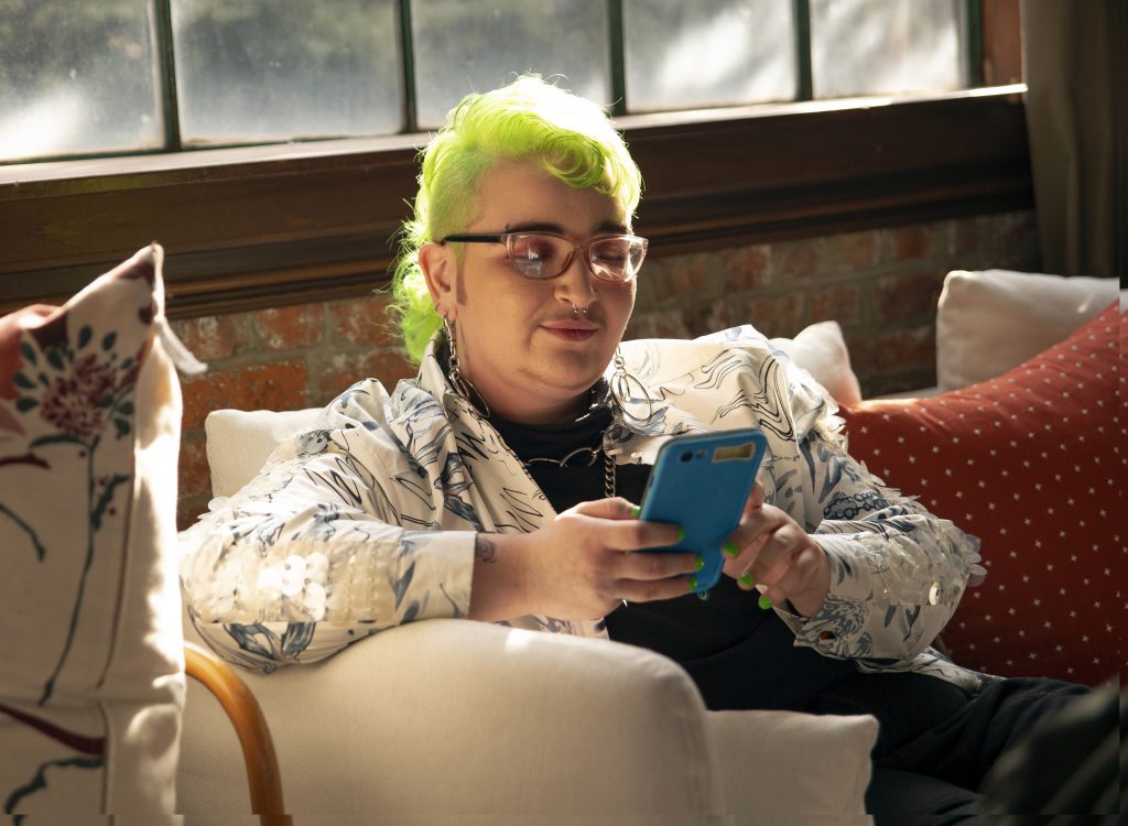 Person with green hair looking and smiling at a phone.
