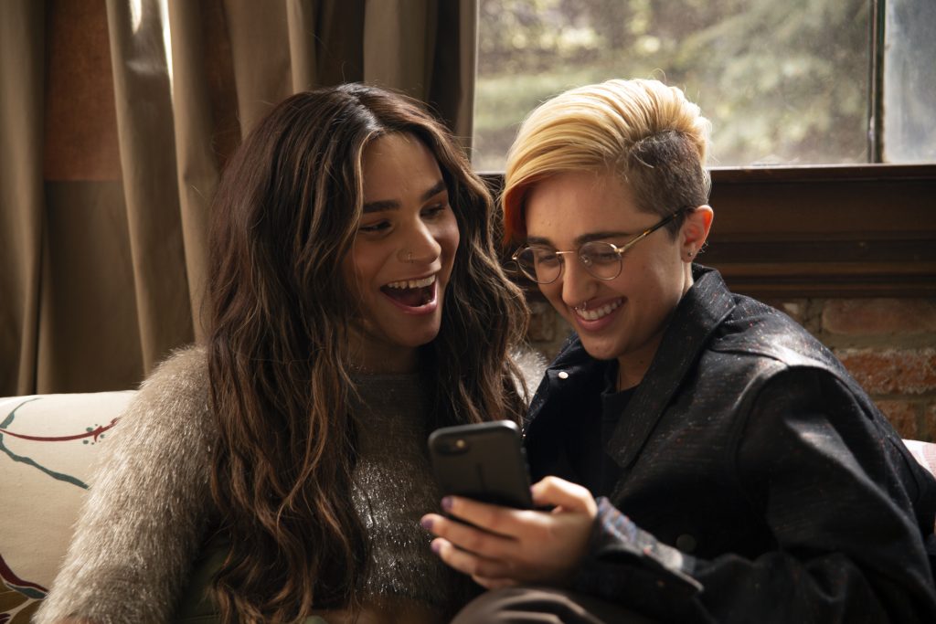Two persons smiling while looking at a phone screen.
