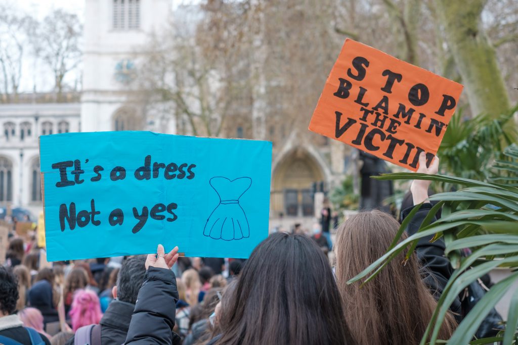 People holding signs that say "It's a dress not a yes" and "Stop blamin' the victim."