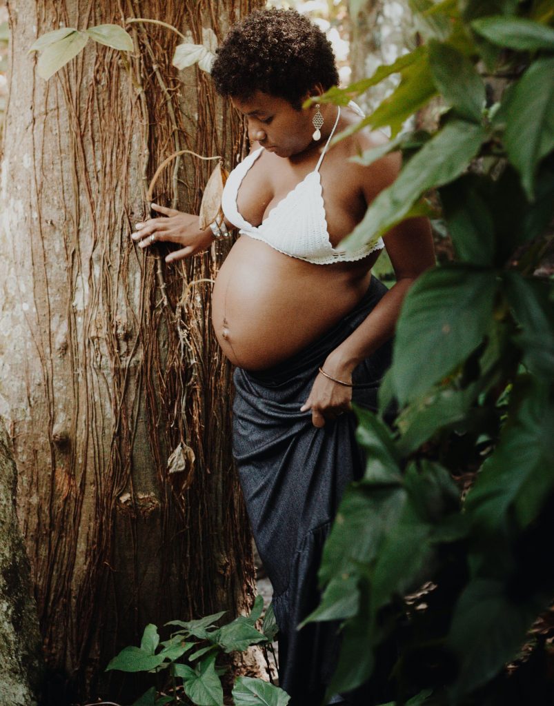Pregnant woman standing beside a tree.