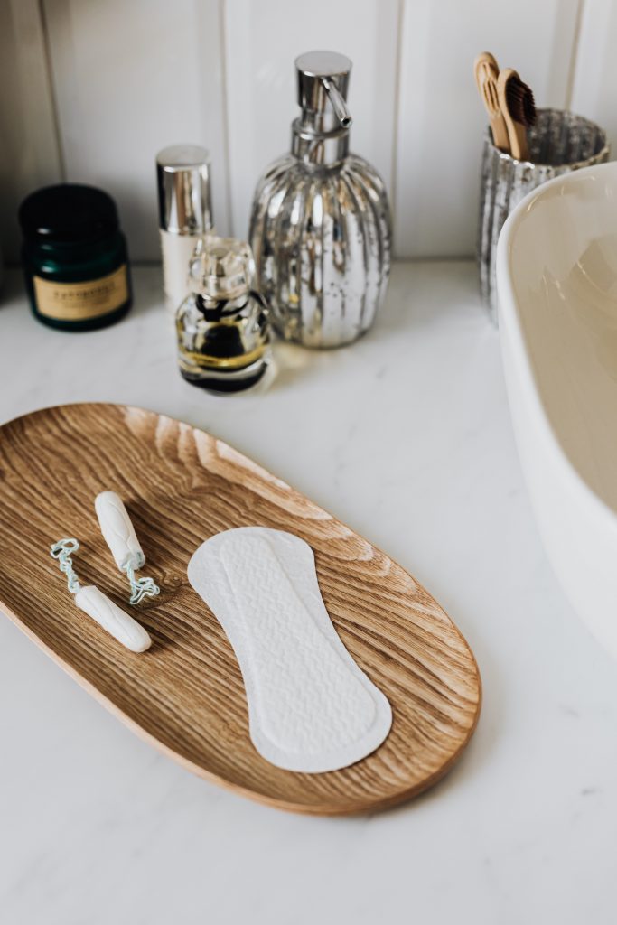 A menstrual pad and tampons on top of a wooden plate.