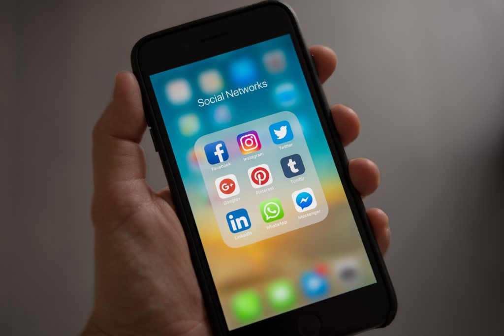 A phone with six social media apps: Facebook, Instagram, Twitter, Google, Pinterest, Twitter, LinkedIn, WhatsApp, and Messenger.