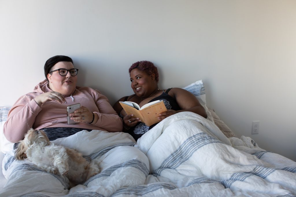 A plus size couple laying on a bed, smiling at each other.