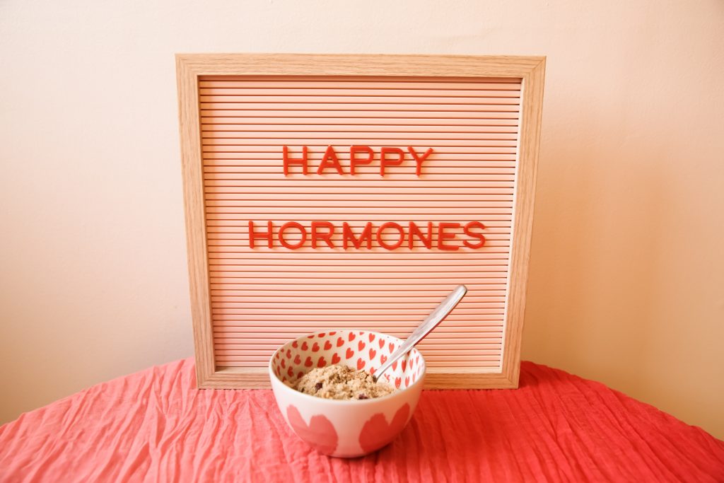 "HAPPY HORMONES" spelled out on a squared frame. There is a bowl of ice cream in front of the frame.