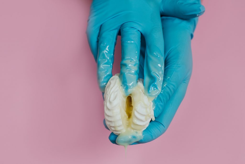 A person's hands in gloves holding an object that resembles a vagina. There is a milky substance coming out of the object that resembles a vagina.