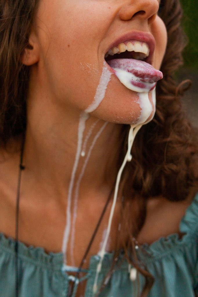 A person sticking out their tounge. There is a milky substance dripping from the person's tounge, mouth, and neck.