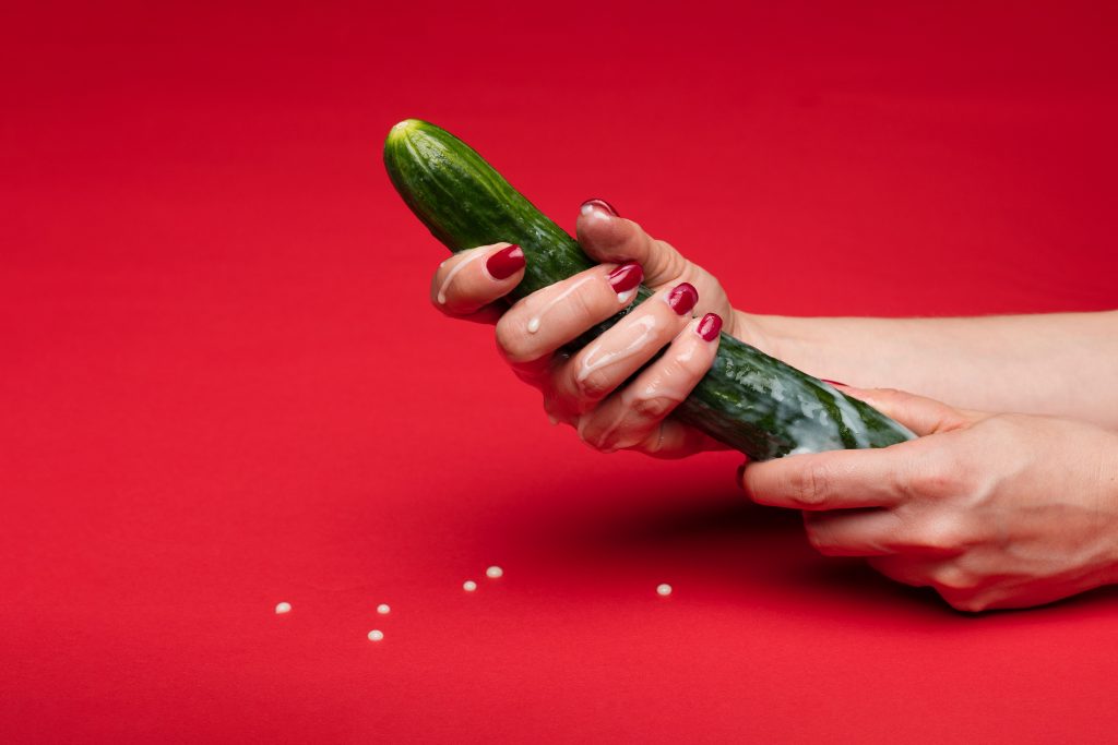 A person holding a cucumber that resembles a penis. There is a milky substance on the cucumber.