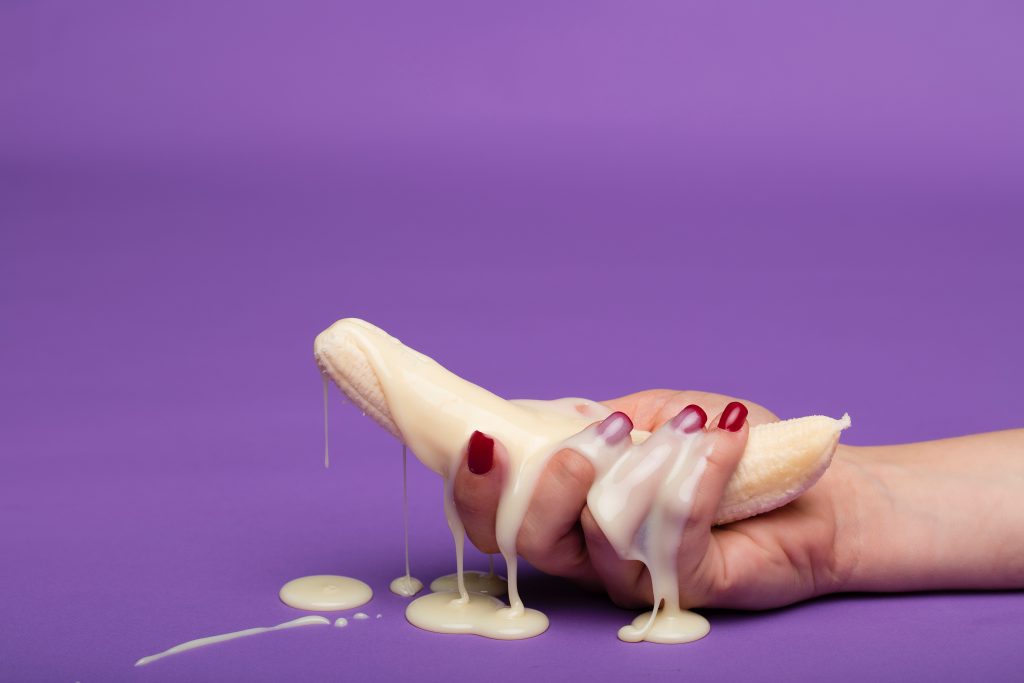 A person holding a banana covered in a milky substance.