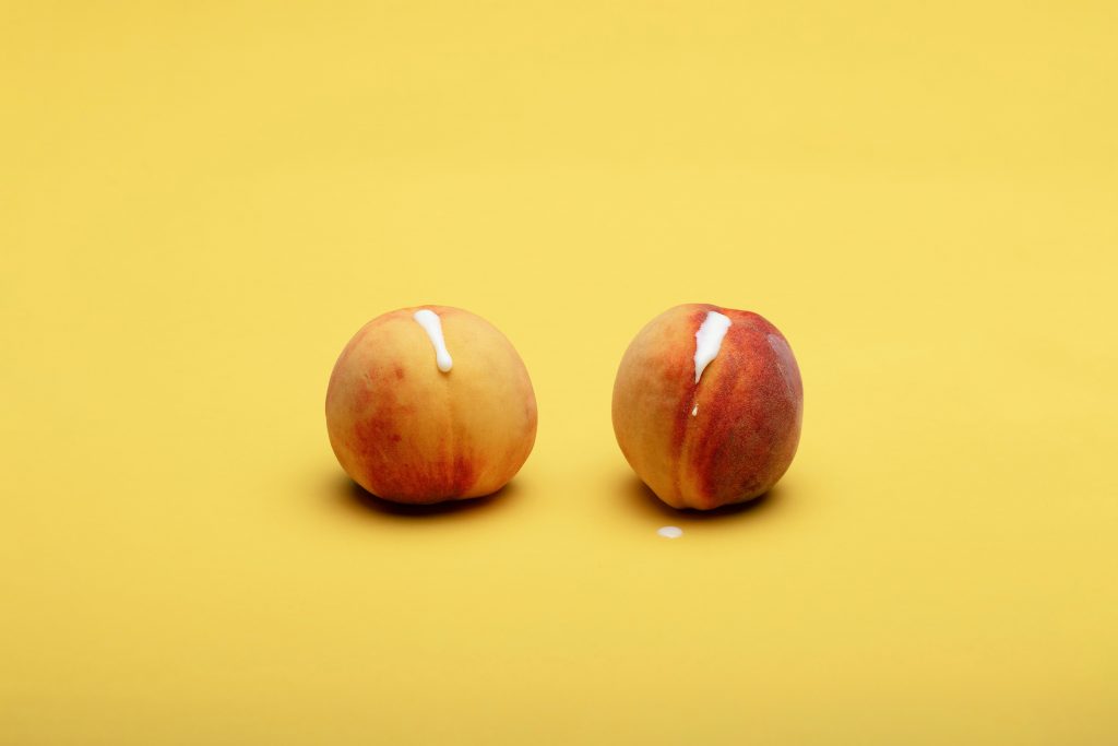 Two nectarines resembling vaginas. There is a milky substance dripping out the middle of the nectarines.
