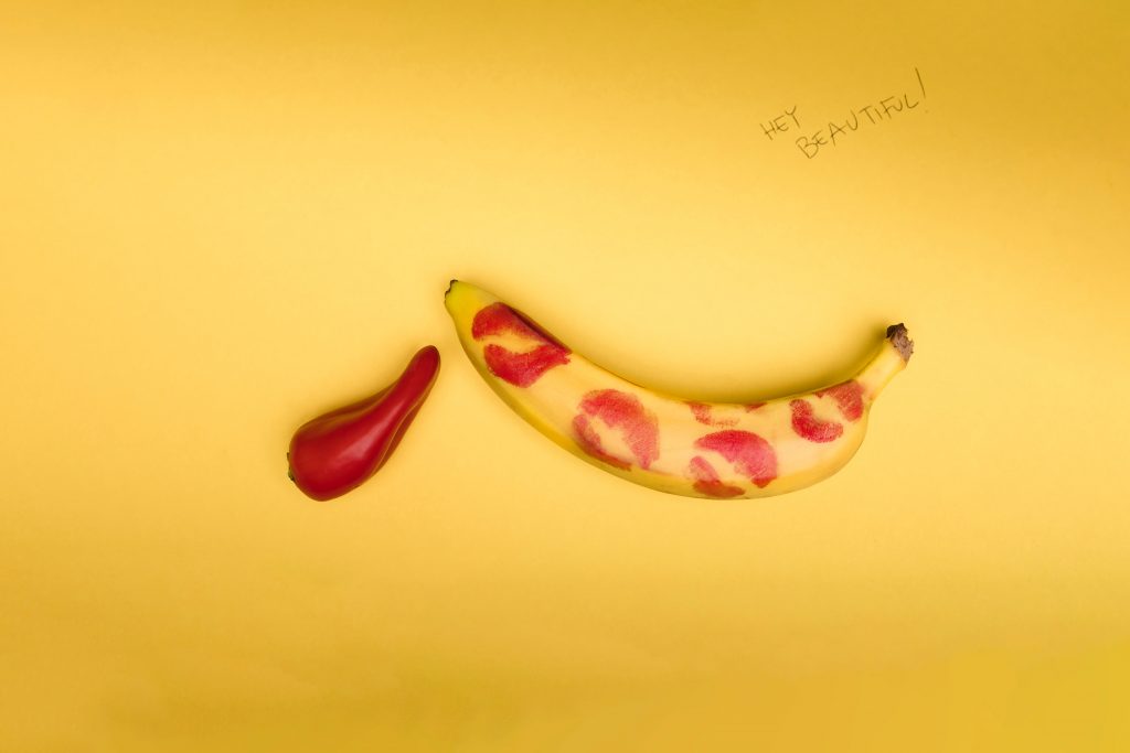 A bell pepper next to a banana that has red kiss stains on it.