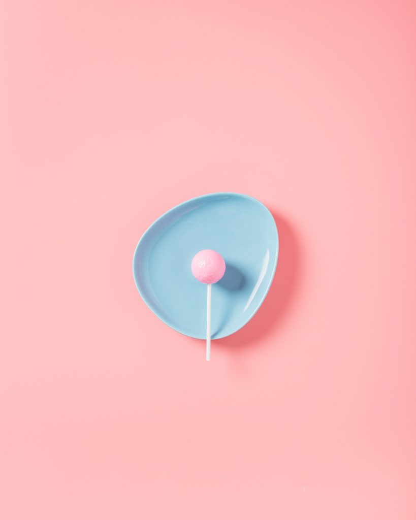 a pink lollipop on a baby blue plate with a light pink background