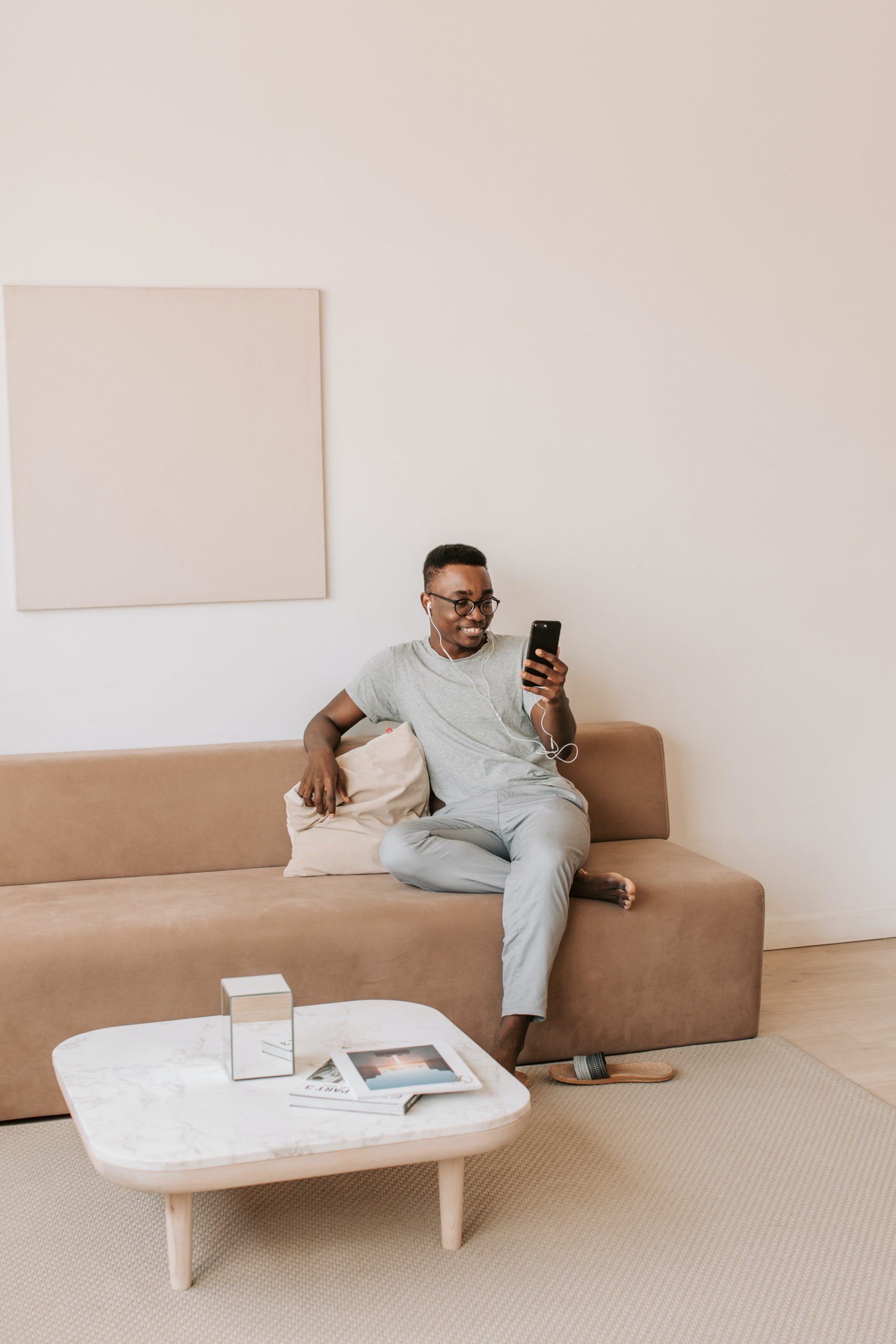 A person sitting on a couch. The person is smiling at their phone and wearing earphones.