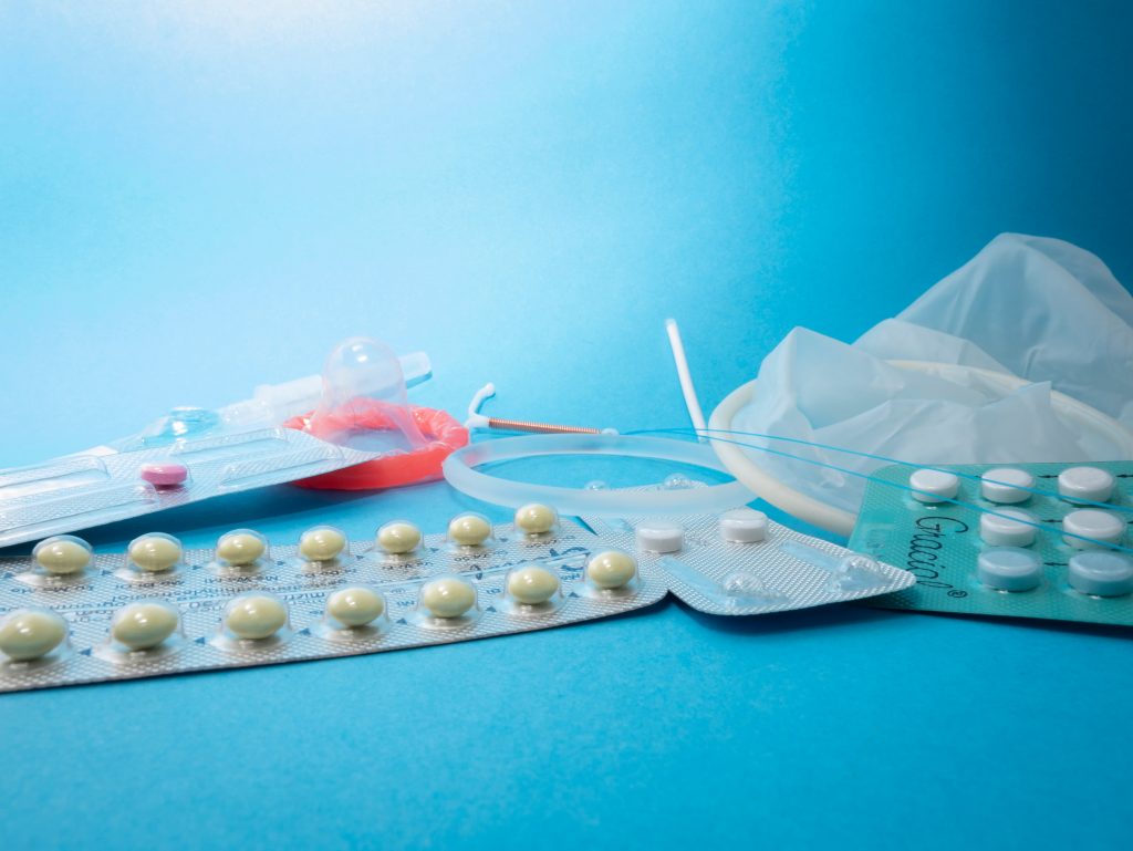 A variety of contraceptive methods: birth control pills, condoms, arm implants, and vaginal ring.